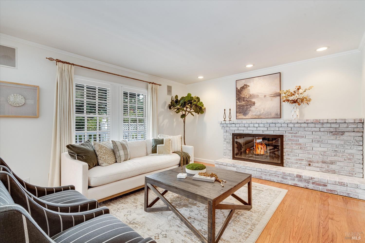 Staged living room with a lit white-brick fireplace, white sofa, and dark striped armchairs.