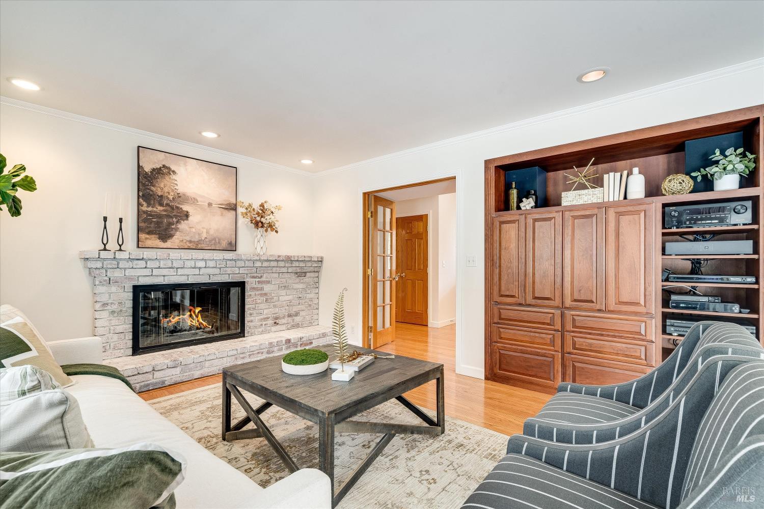 Living room with a white brick fireplace, built-in walnut cabinetry, and striped chairs.