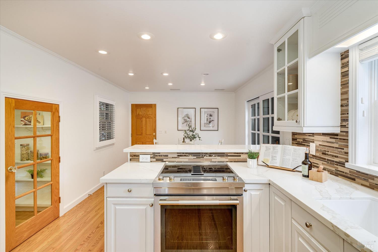 Bright kitchen with white cabinets, a stainless steel range, patterned tile backsplash, and glass-paneled wood door.