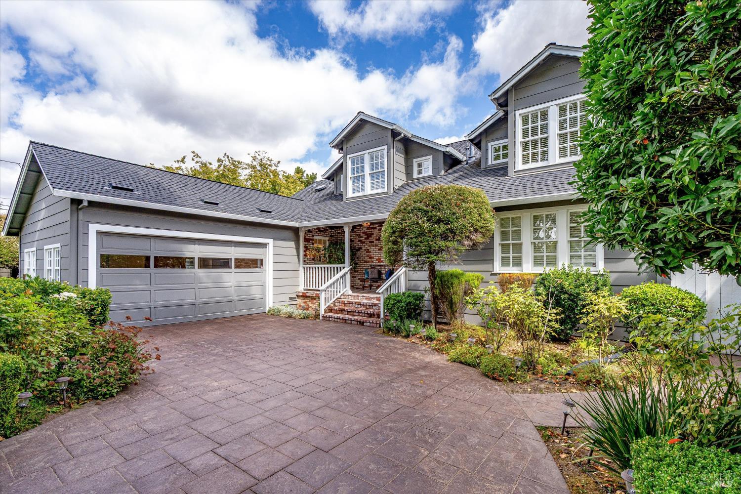 Gray two-story home with a large garage, brick entry porch, and landscaped front garden.