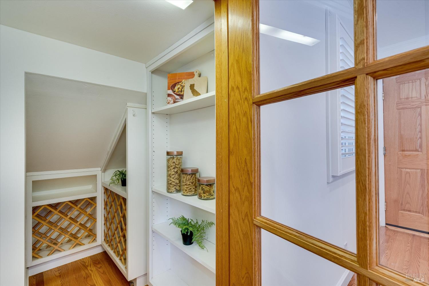 Walk-in pantry with built-in wine racks and white shelves stocked with jars and plants.