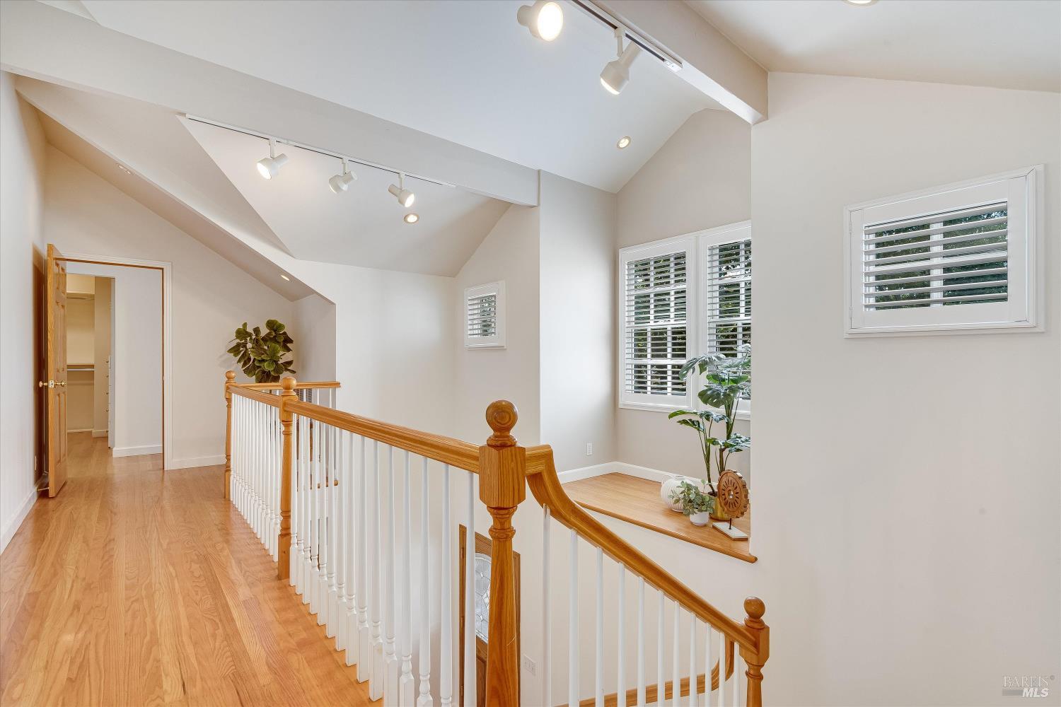 Upstairs landing with a vaulted ceiling, hardwood floors, and a curved wooden-and-white stair railing.