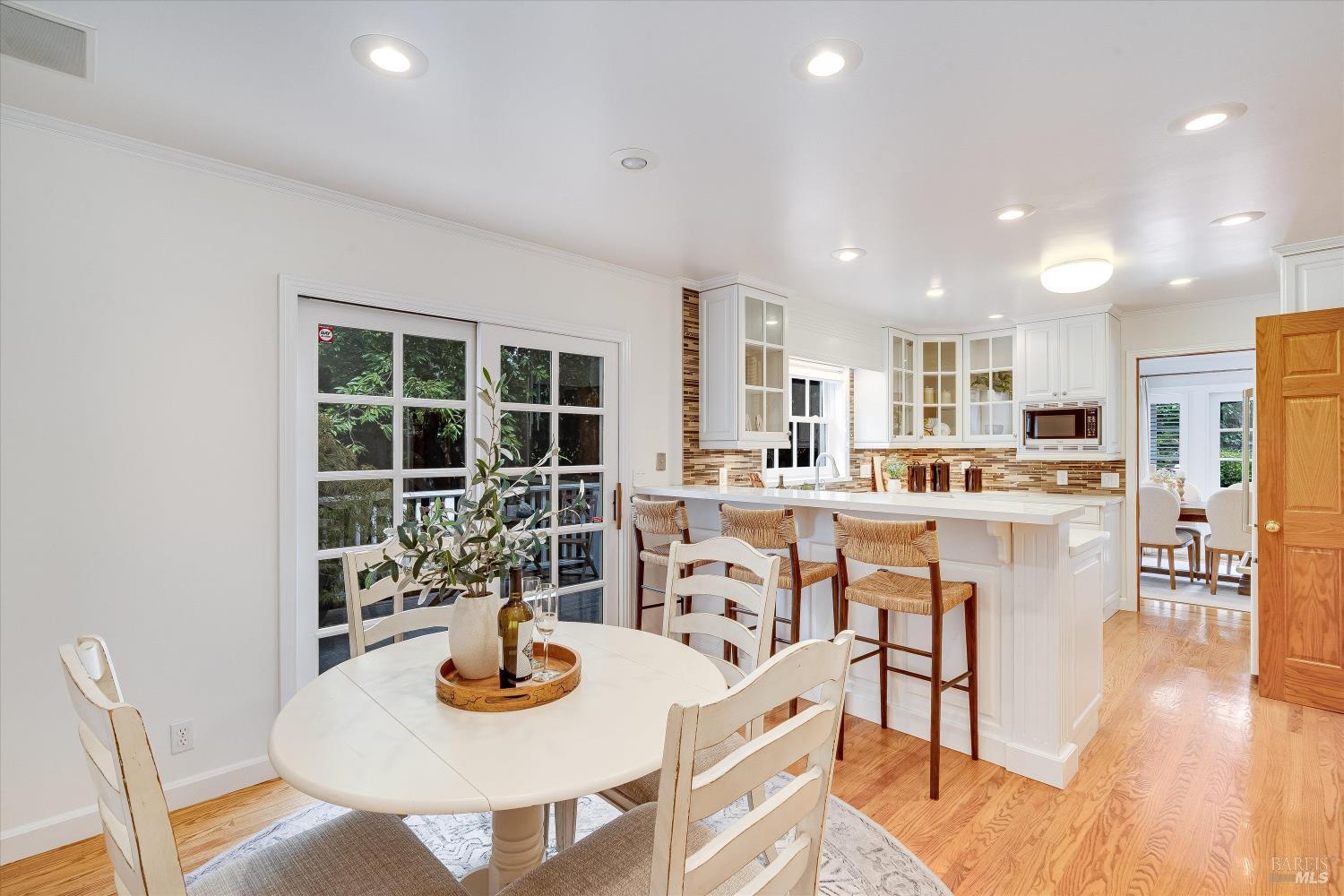 Kitchen and dining area with a large island, white cabinetry, woven bar stools, and sliding glass doors.