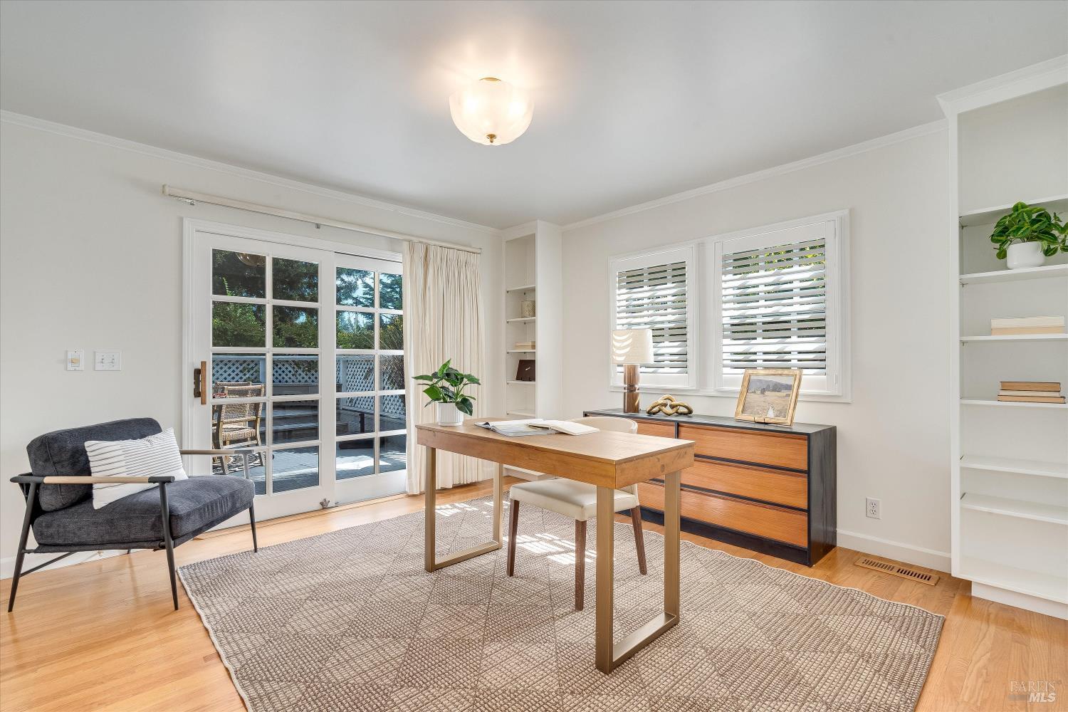 Bright home office with a wooden desk, built-in shelving, and sliding glass doors to a deck.