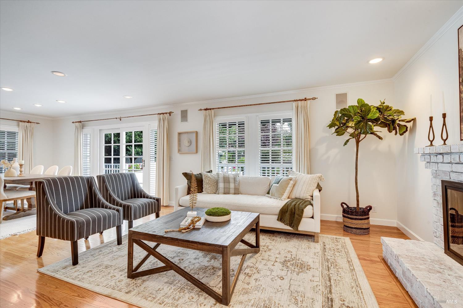 Living room with a white sofa, striped armchairs, hardwood floors, and a white brick fireplace.