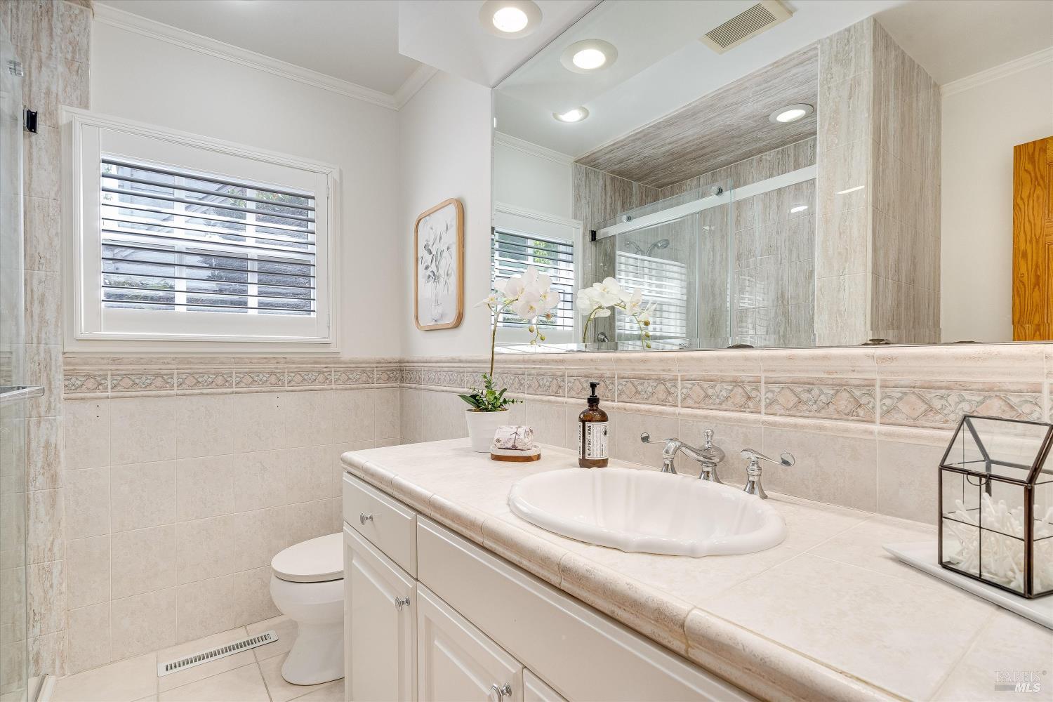 Bright tiled bathroom with a long vanity, large mirror, and glass-enclosed shower.