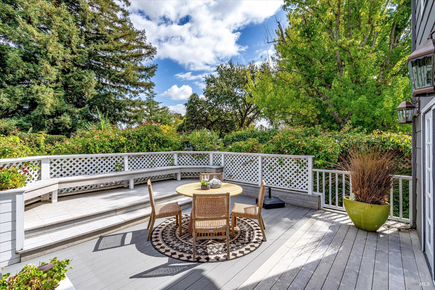 Outdoor deck with round dining set, built-in bench seating, white lattice railings, and surrounding trees.