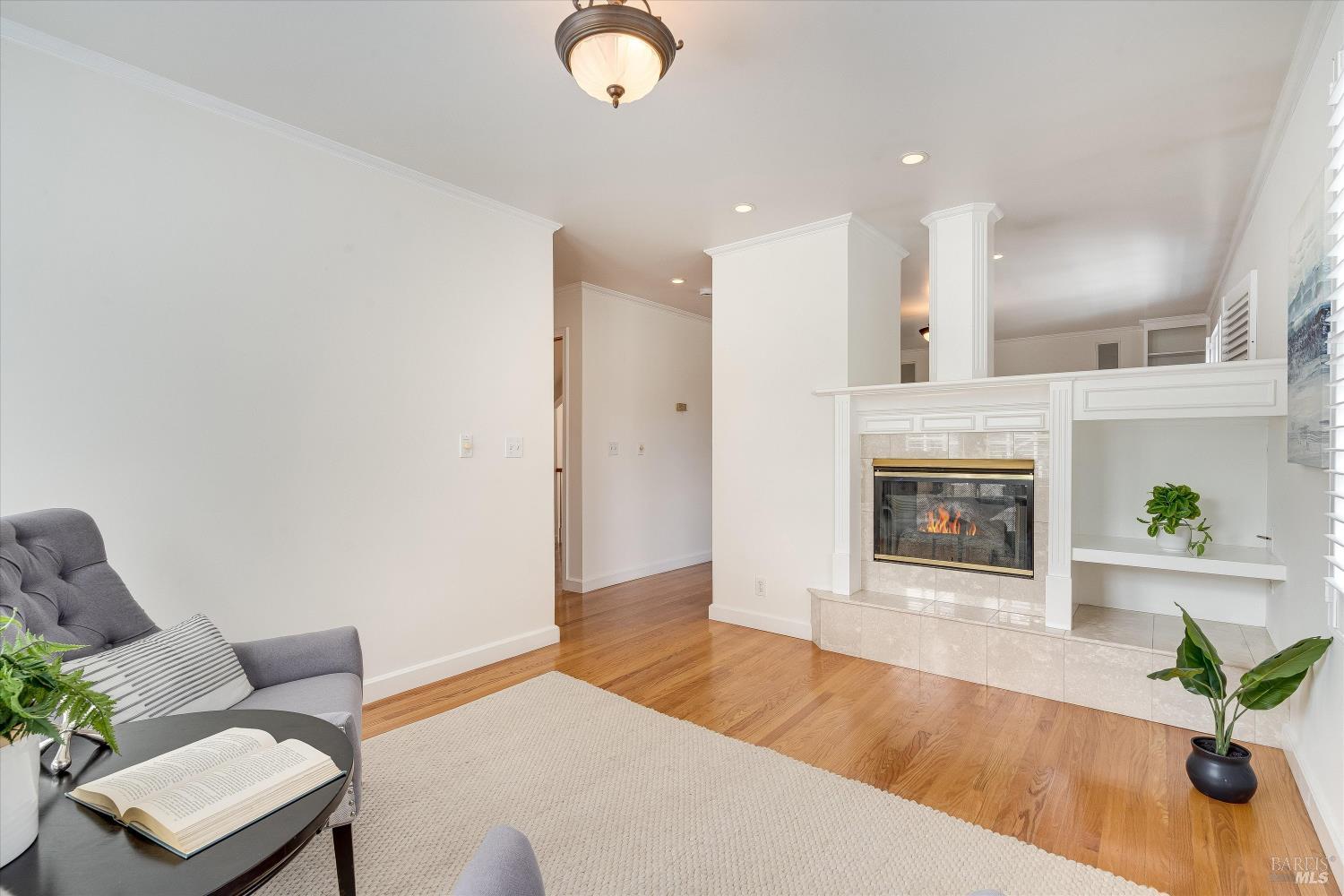 Furnished living room with a lit fireplace, hardwood floors, and built-in shelving.
