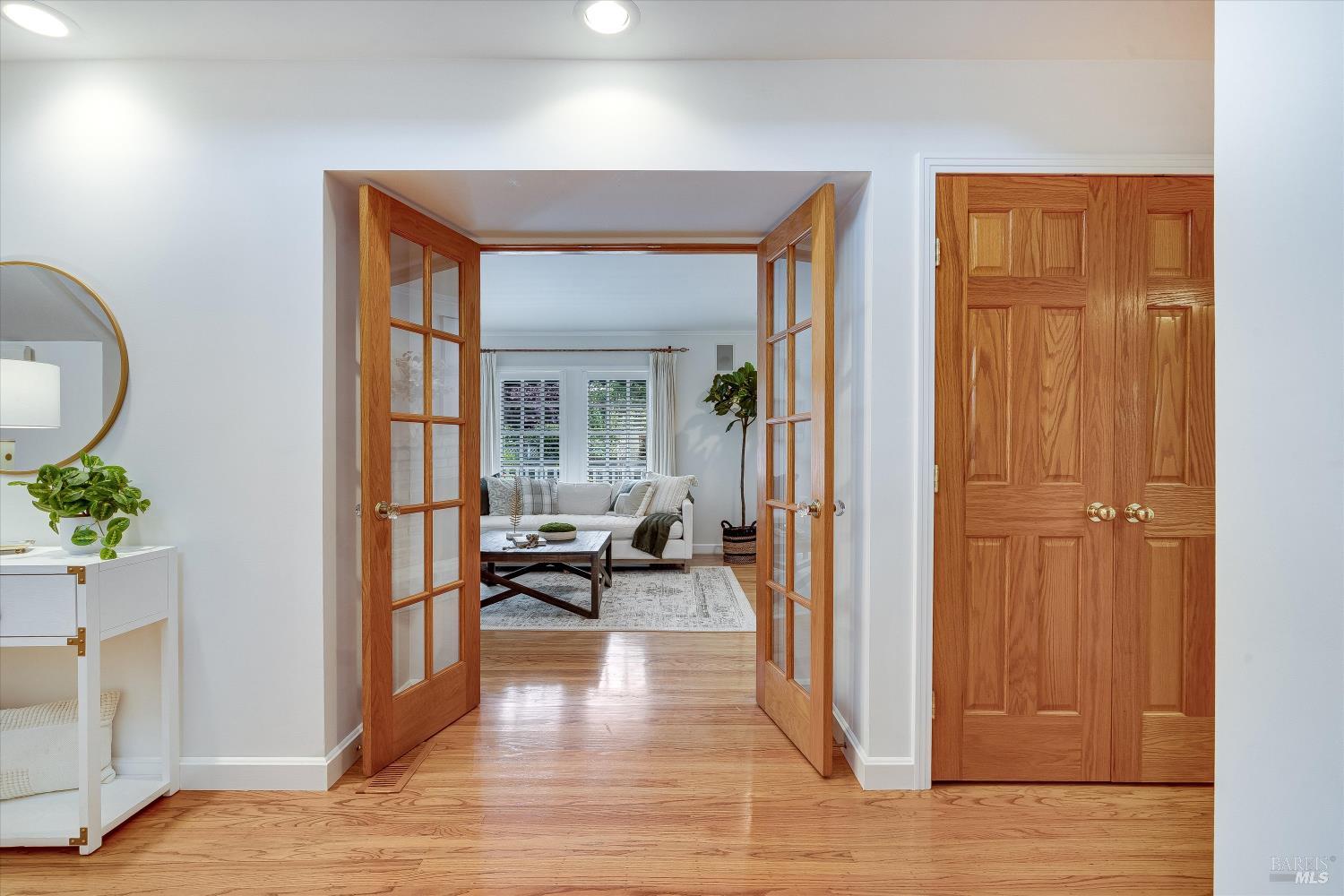 Hallway with hardwood floors and open French doors leading to a bright living room.