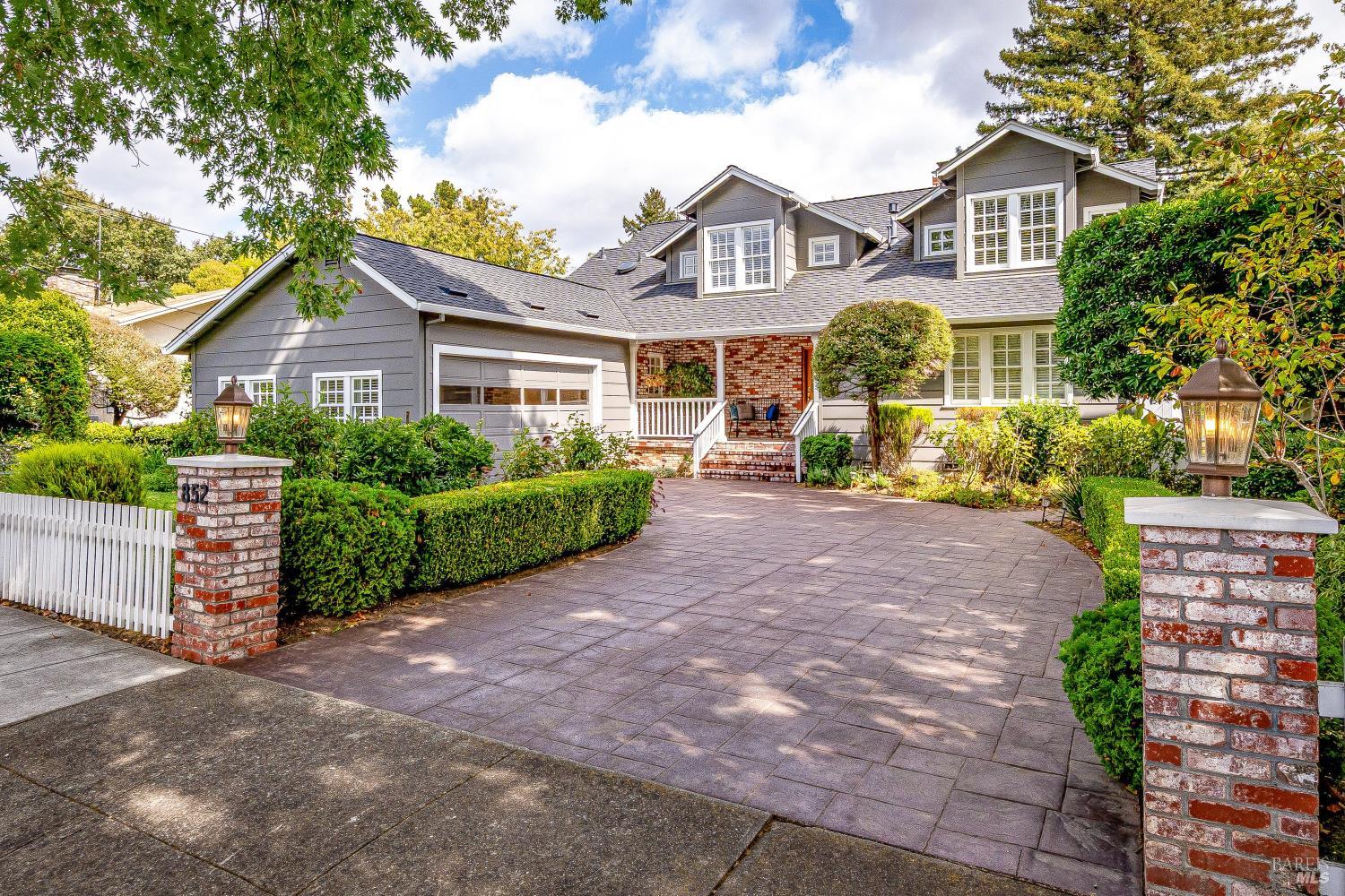 Gray two-story home with a broad paved driveway, brick entry, and landscaped gardens.