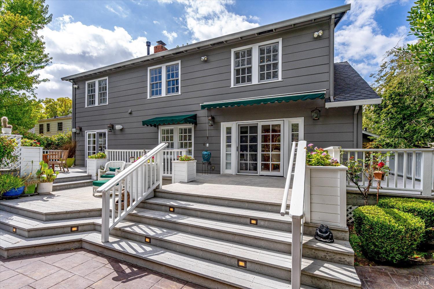 Gray two-story home with green awnings and a spacious white-railed multi-level deck.