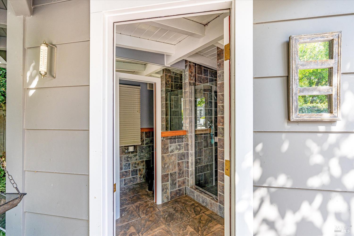 Bathroom with a glass-enclosed, stone-look tiled shower, viewed through an open doorway.