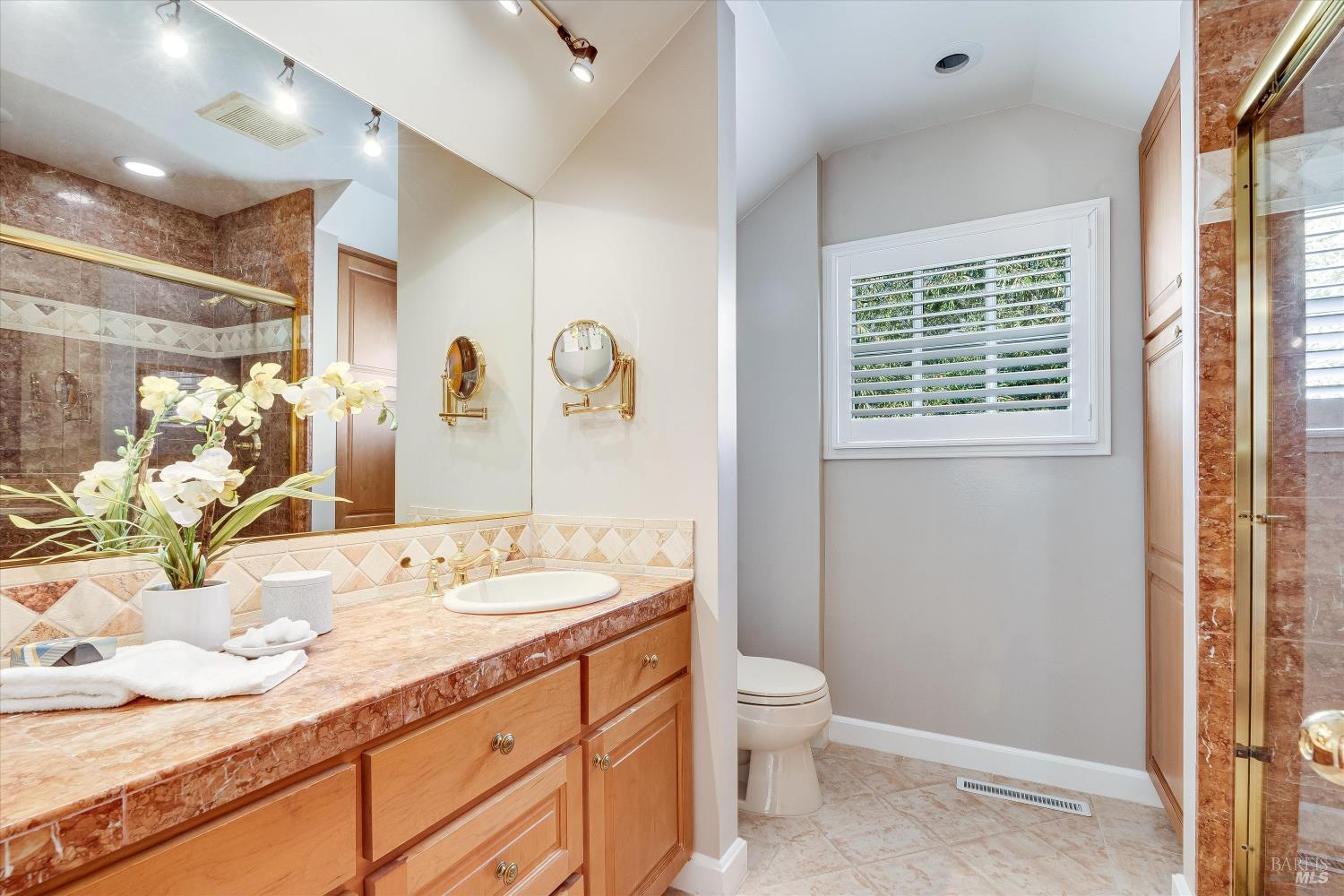 Bathroom with a wood vanity and stone counter, beside a toilet under a shuttered window.
