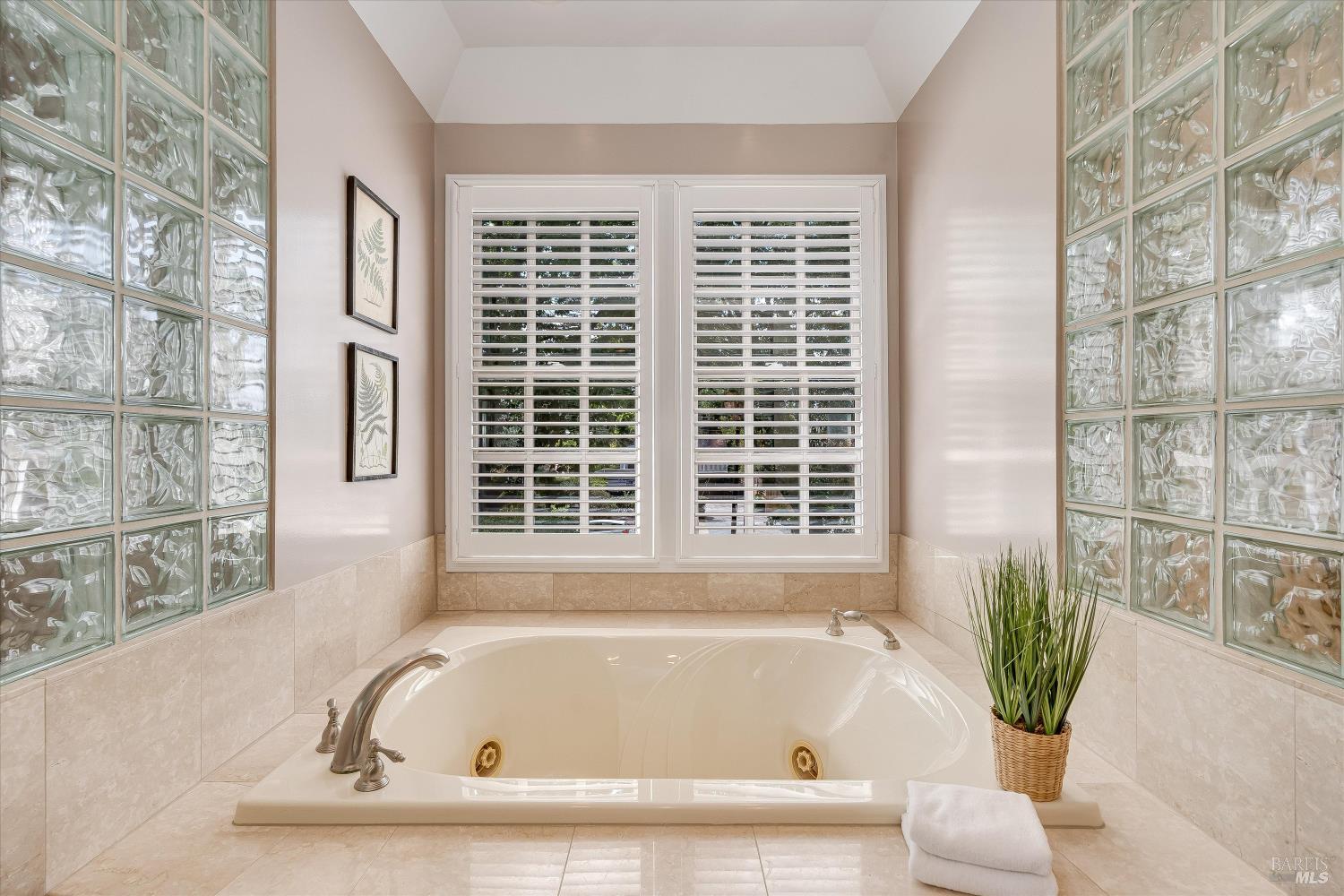 Bathroom with a built-in soaking tub, glass-block walls, and plantation-shuttered windows.