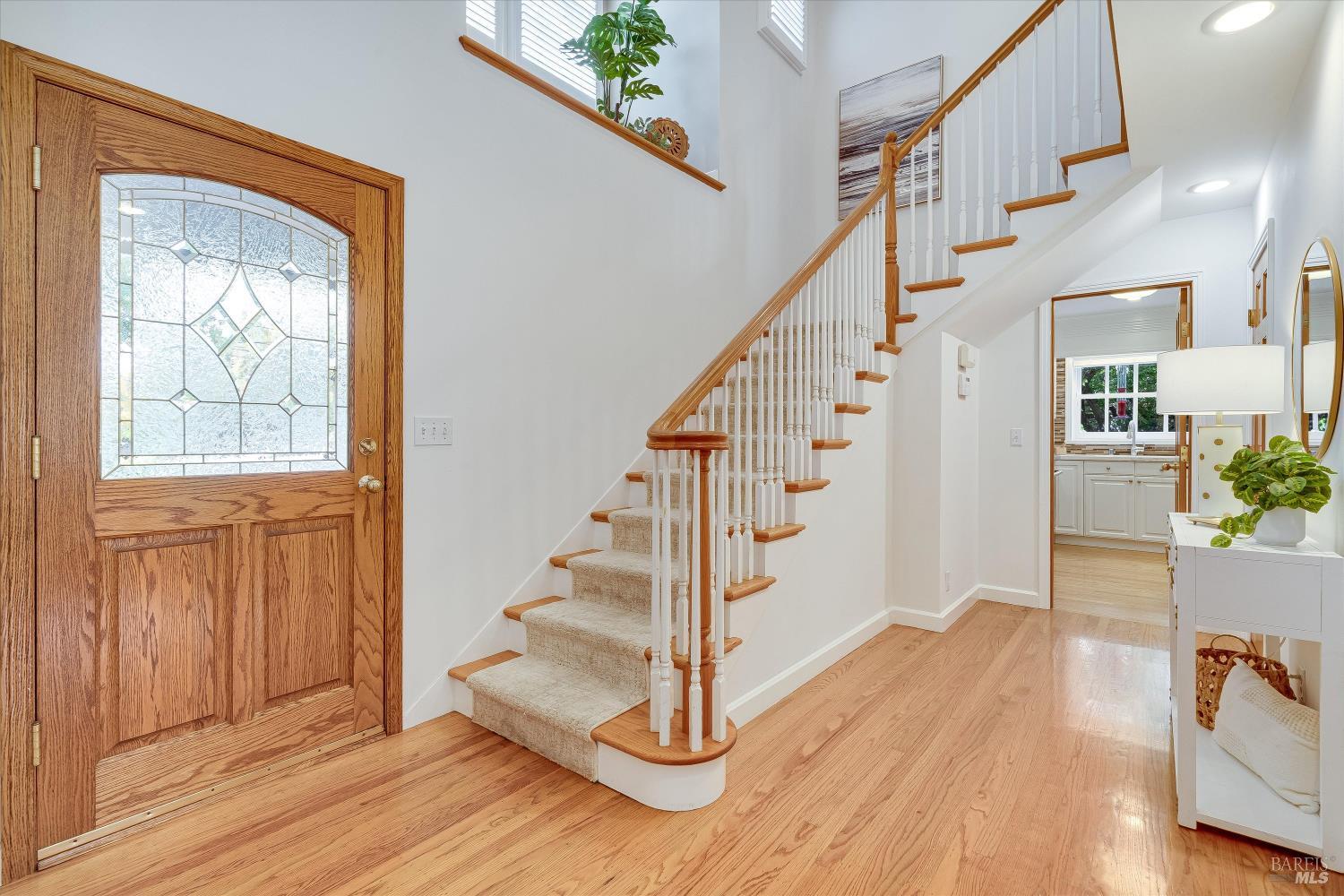 Entry foyer with a leaded-glass wood door, carpeted staircase, and hardwood floors.