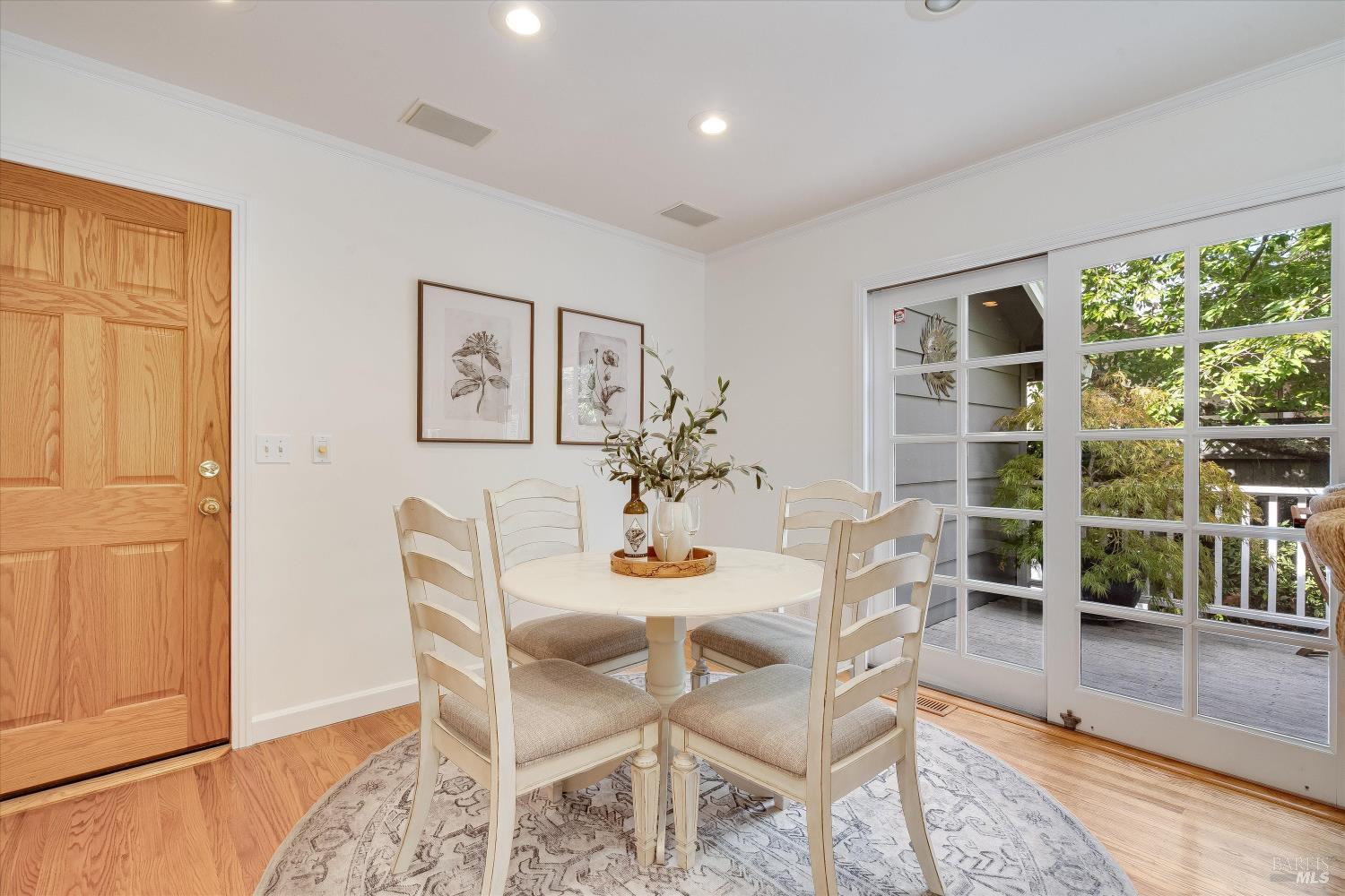 Dining room with a round table, upholstered chairs, and glass doors opening onto a leafy patio.