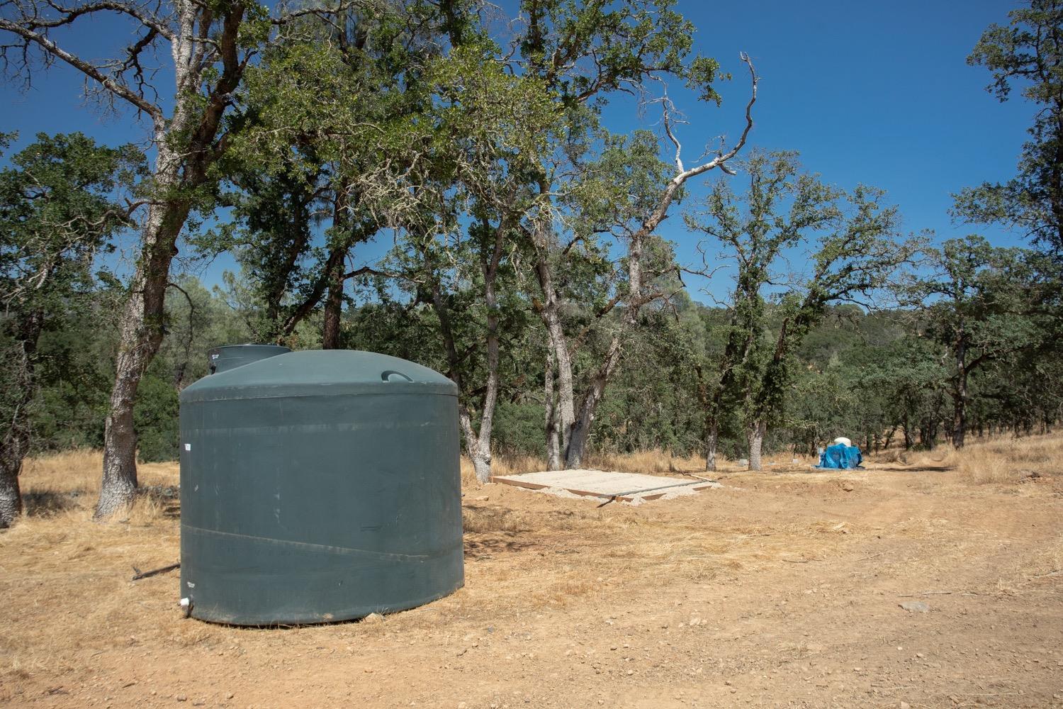 Rural property with a large water tank, dry ground, and mature oak trees.