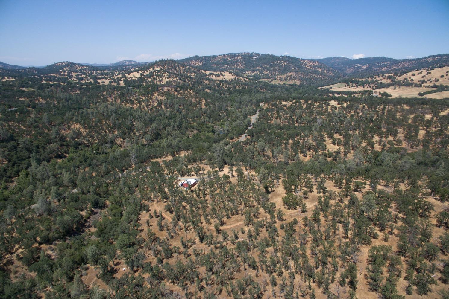 Aerial view of a red-and-white roofed building surrounded by wooded, rolling hills.