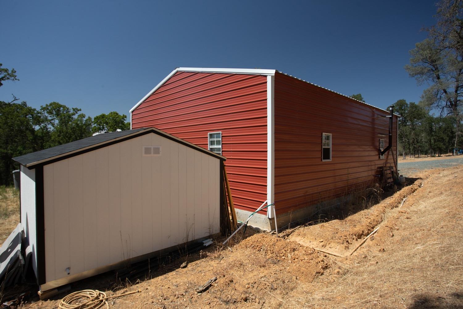 Red metal barn and beige shed on a dry, sloping rural property.