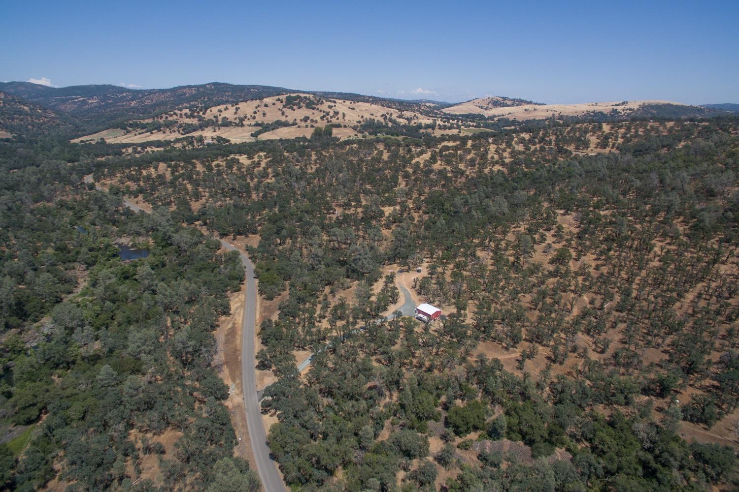 Aerial view of oak-dotted rolling hills, an access road, a red barn, and a small pond.