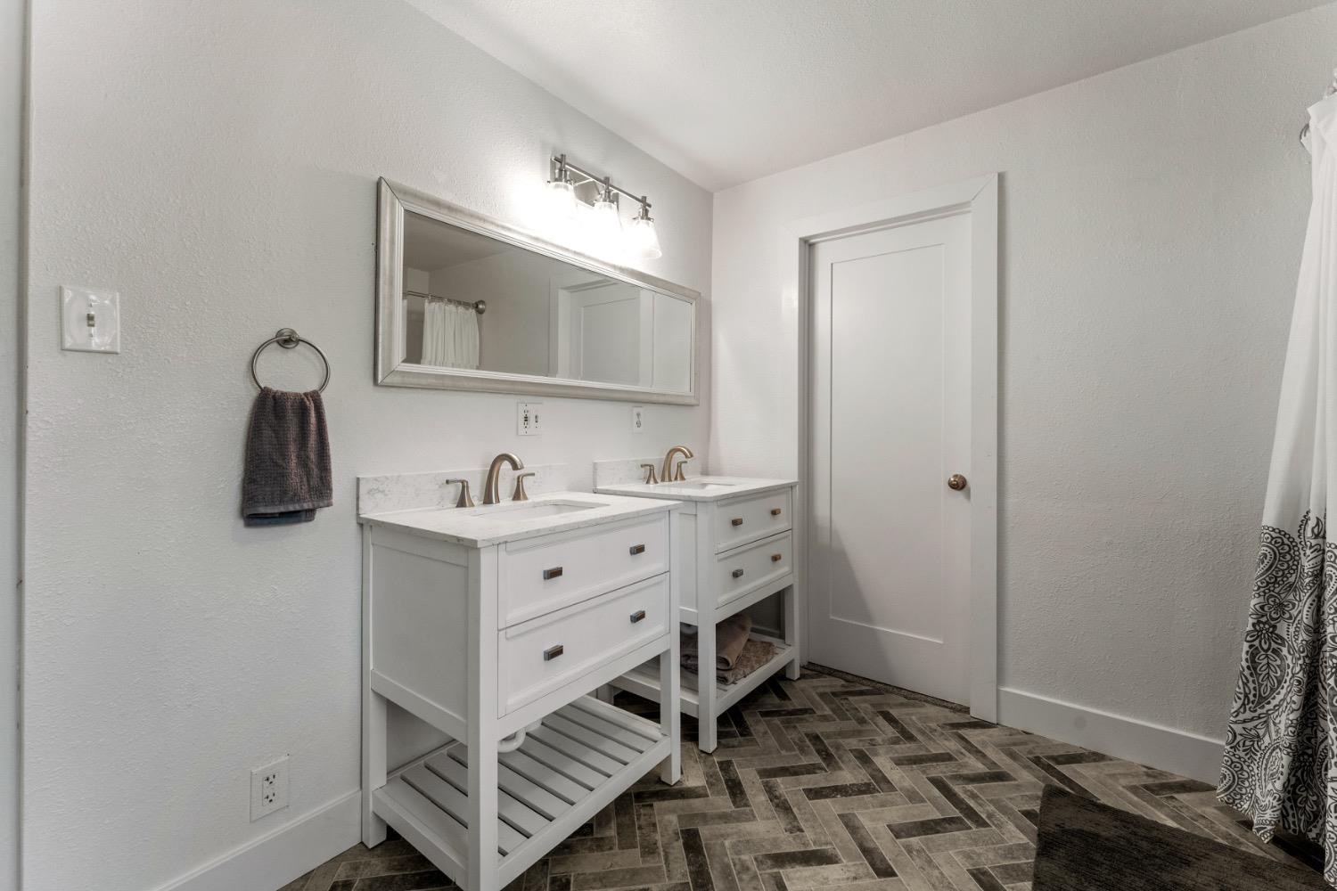 Bathroom with two white vanities, a large framed mirror, and dark herringbone tile flooring.
