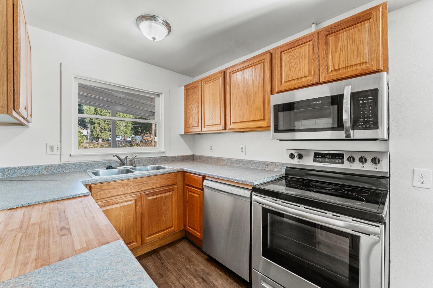 Kitchen with honey-toned cabinets, speckled counters, stainless steel appliances, and a window above the sink.