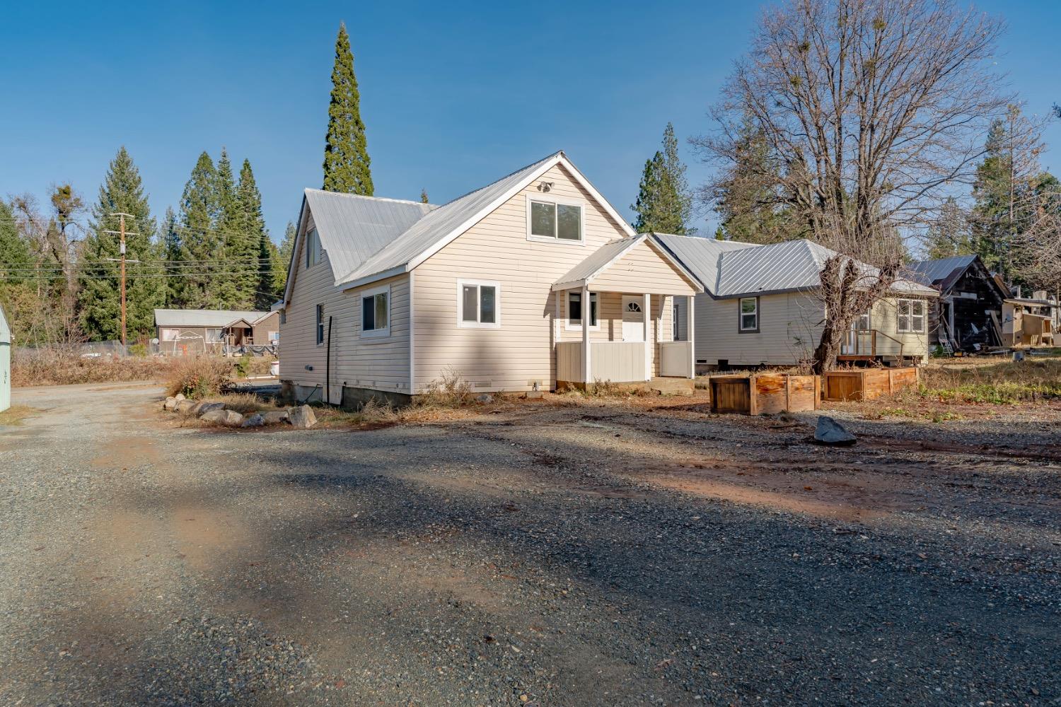 Light-colored home with a metal roof, gravel driveway, raised garden beds, and outbuildings.