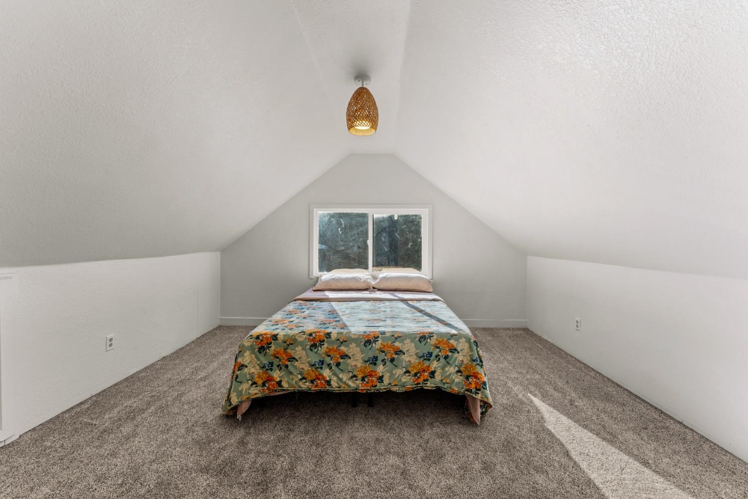 Bedroom with a floral-covered bed beneath a sloped ceiling and window.