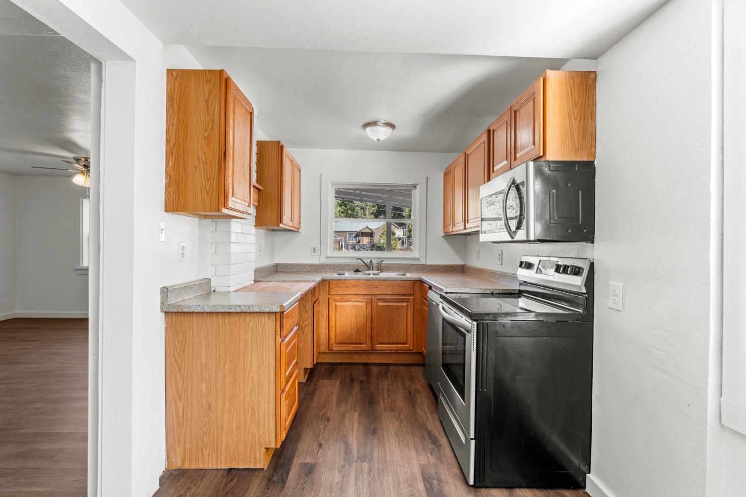 Kitchen with honey-colored wood cabinets, dark appliances, and a window above the sink.