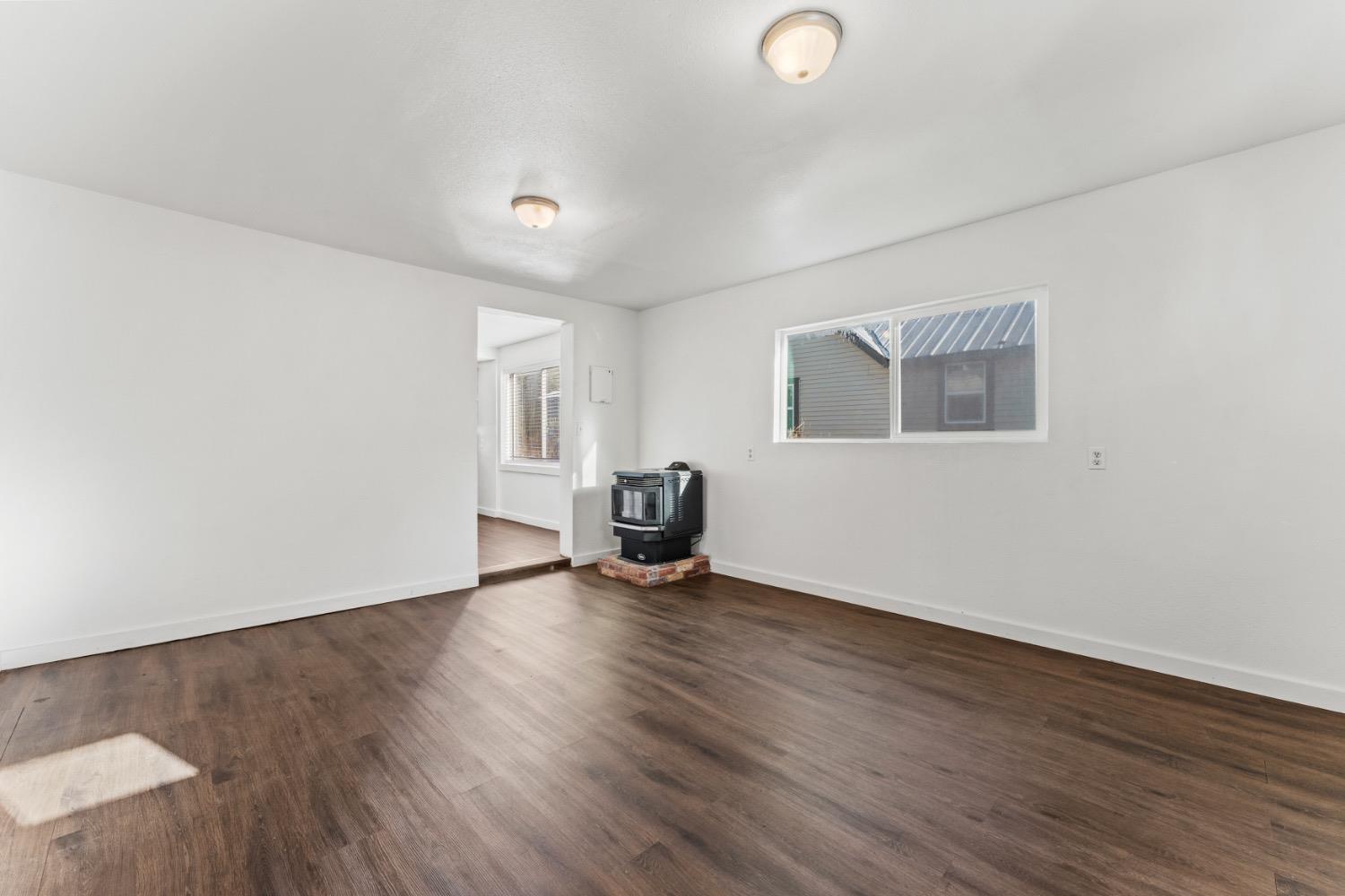 Empty living room with dark wood-look floors and a freestanding stove on a brick hearth.