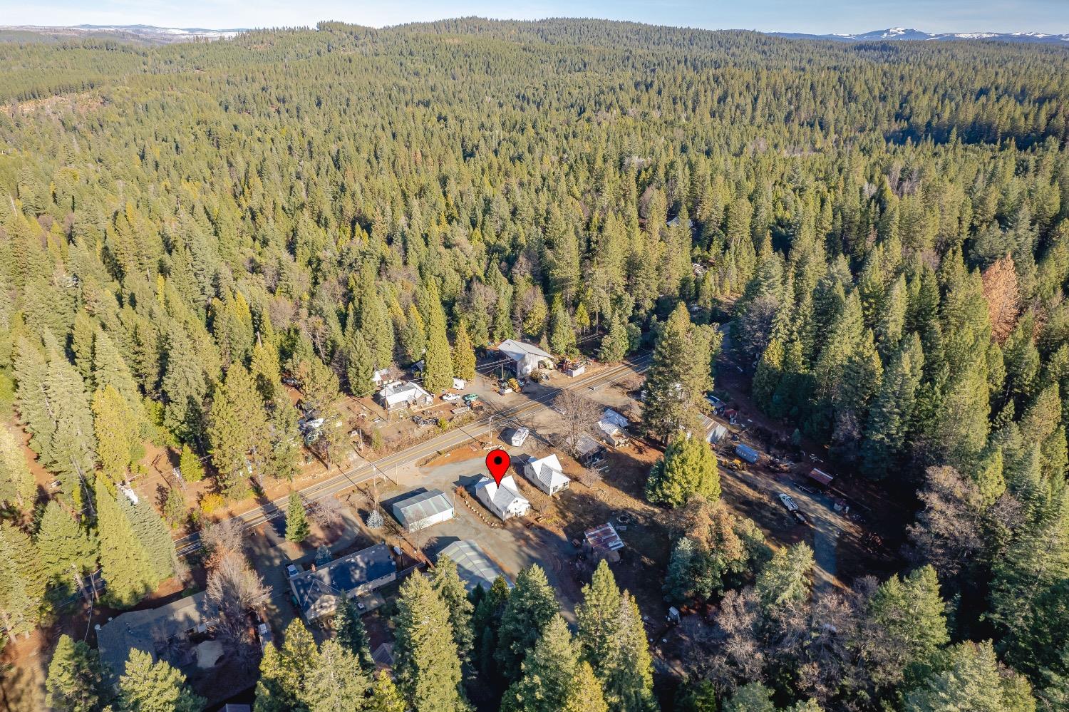 Aerial view of the property along a road, surrounded by dense forest with distant mountain ridges.
