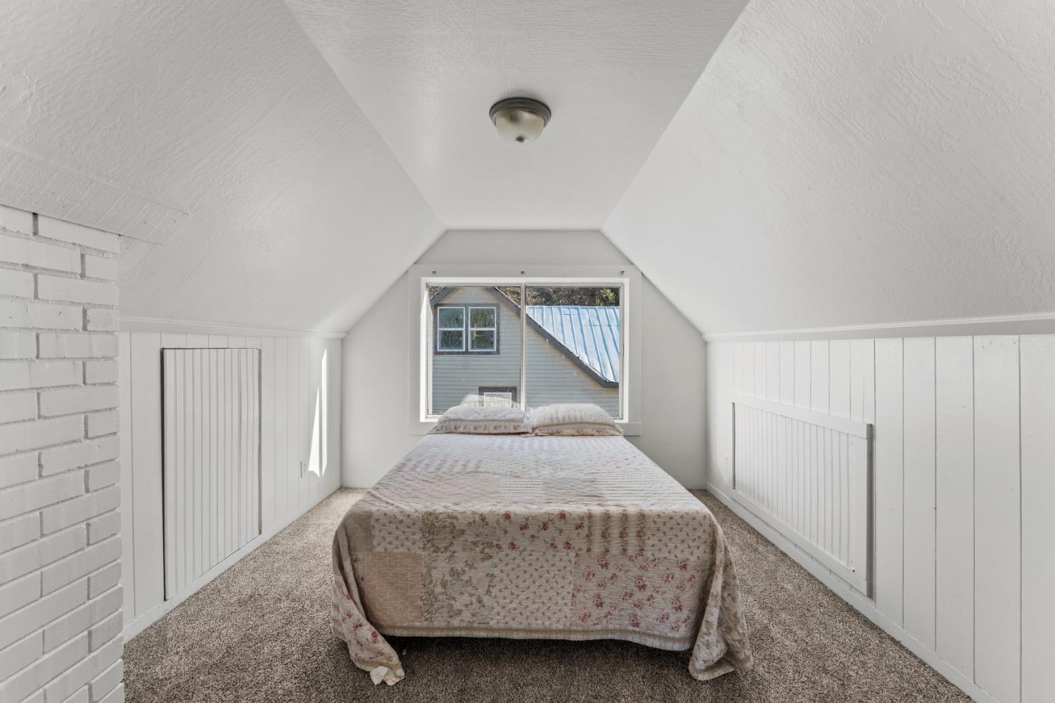Attic bedroom with a floral-covered bed beneath a sloped ceiling and a rear window.