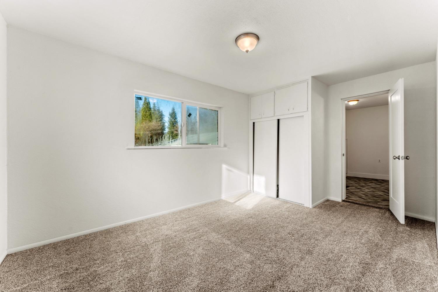Empty bedroom with beige carpet, a small window, and a built-in closet with overhead cabinets.