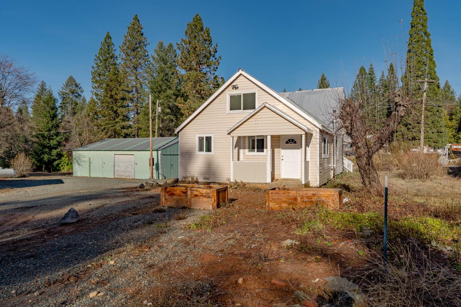 Beige gabled house with a covered entry, green metal outbuilding, and two wooden garden beds.