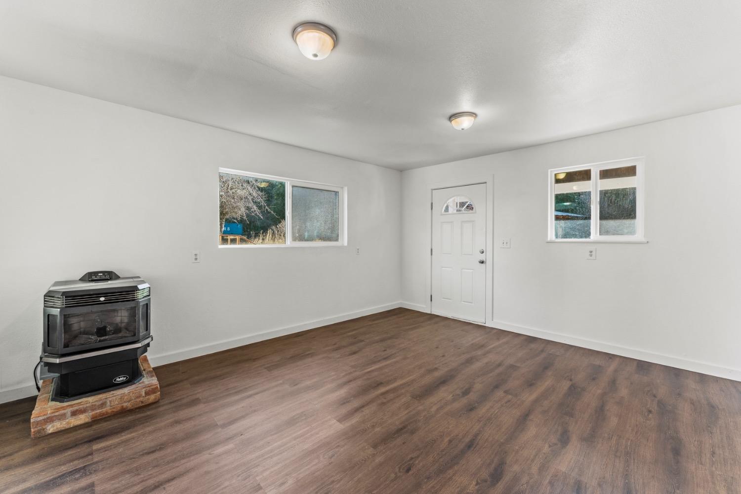 Vacant room with wood-look flooring, two windows, and a freestanding stove on a brick hearth.