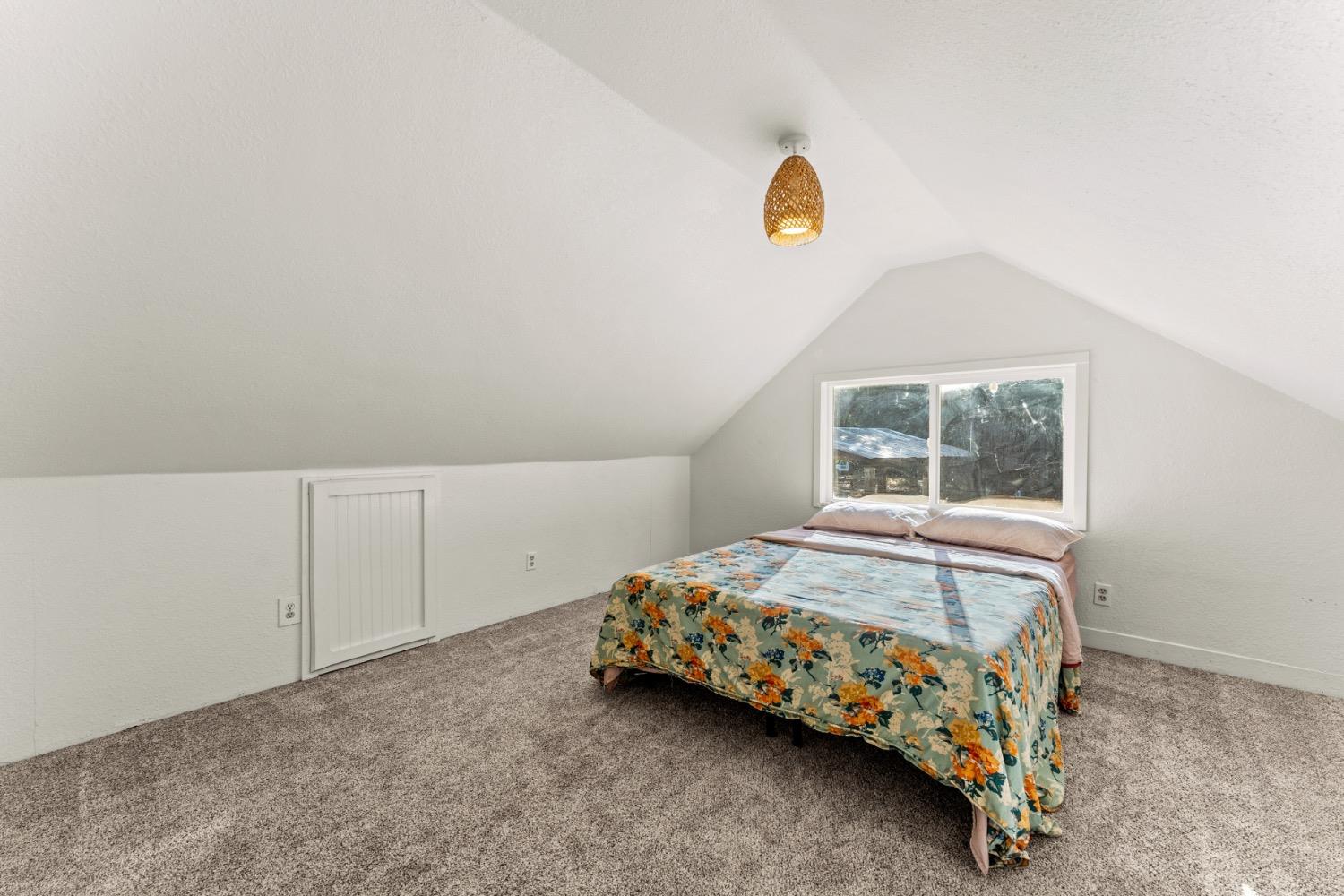 Attic bedroom with a floral-covered bed beneath a window and a sloped ceiling.