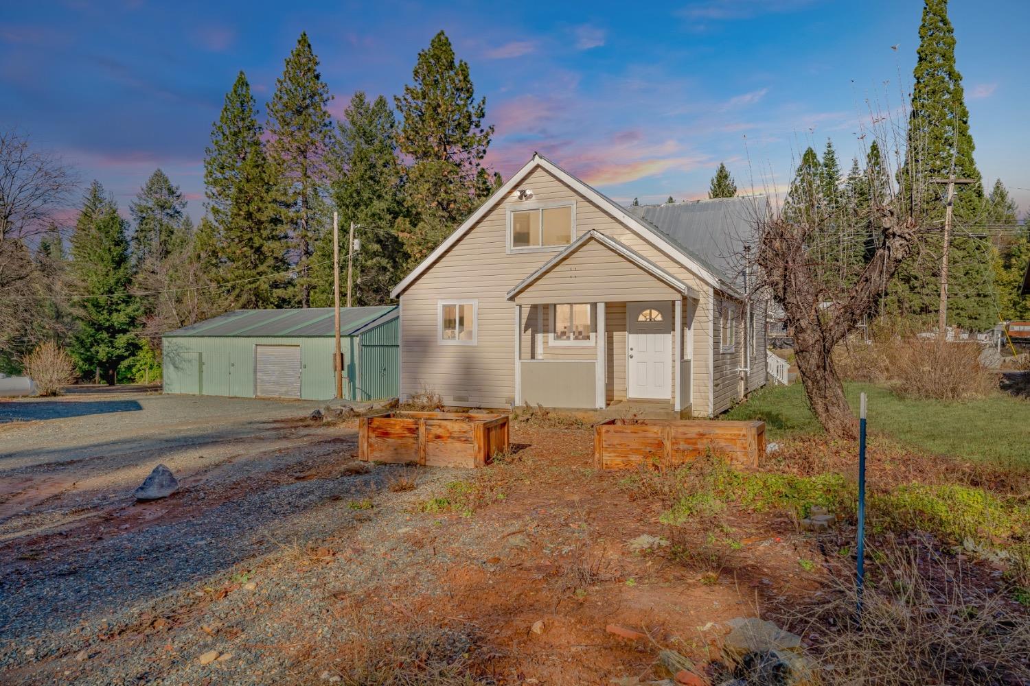 Beige gable-roofed house with a covered entry, green outbuilding, and raised garden beds at dusk.