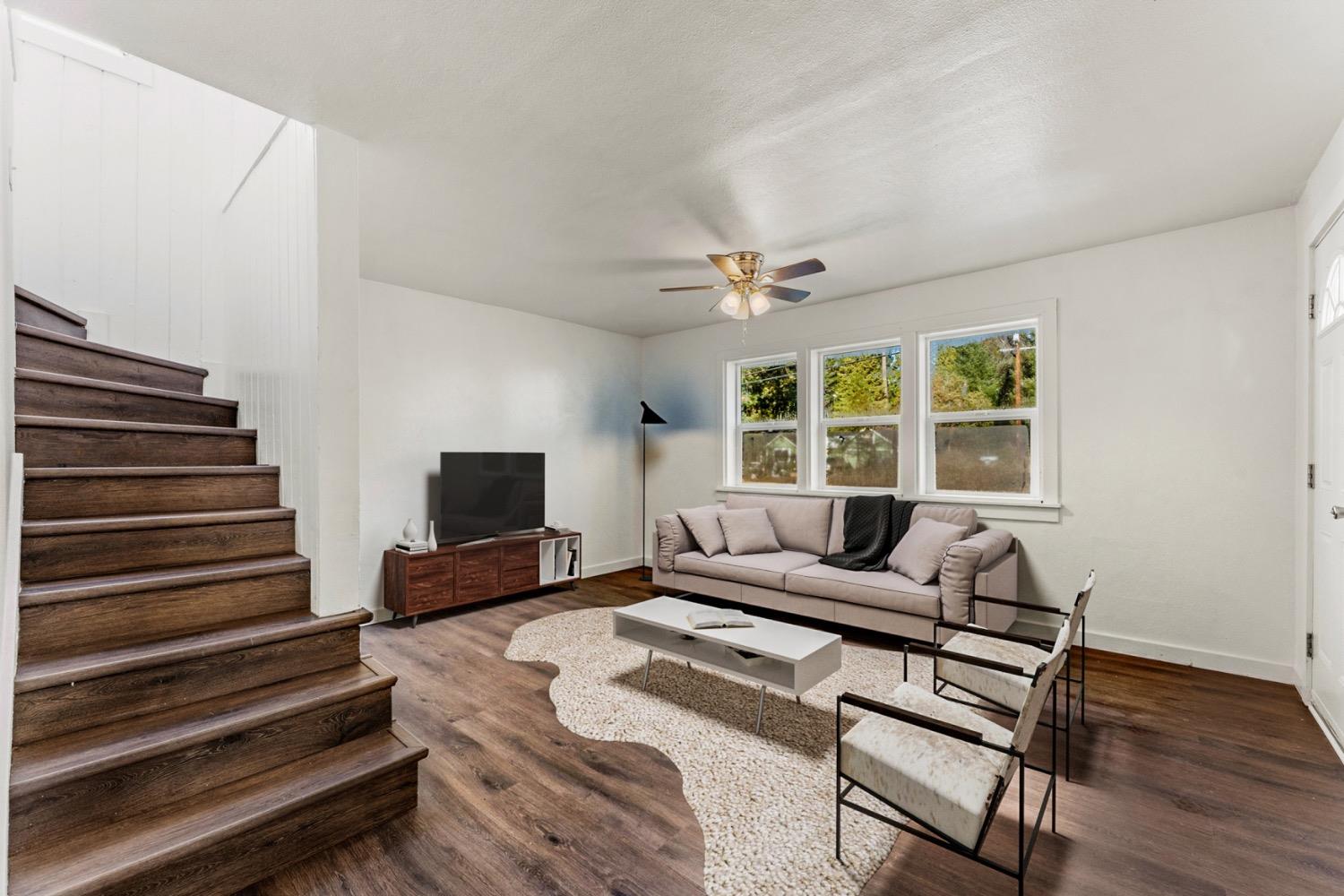Living room with a dark wood staircase, pale sofa, and three windows.