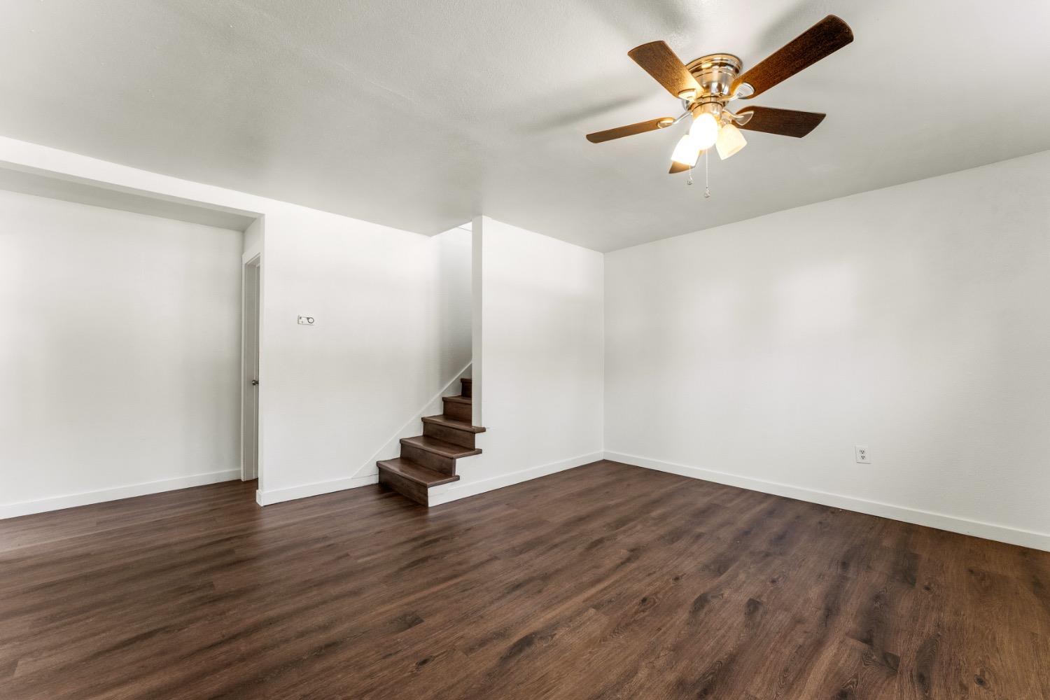 Vacant room with dark flooring, a short staircase, and a ceiling fan with lights.