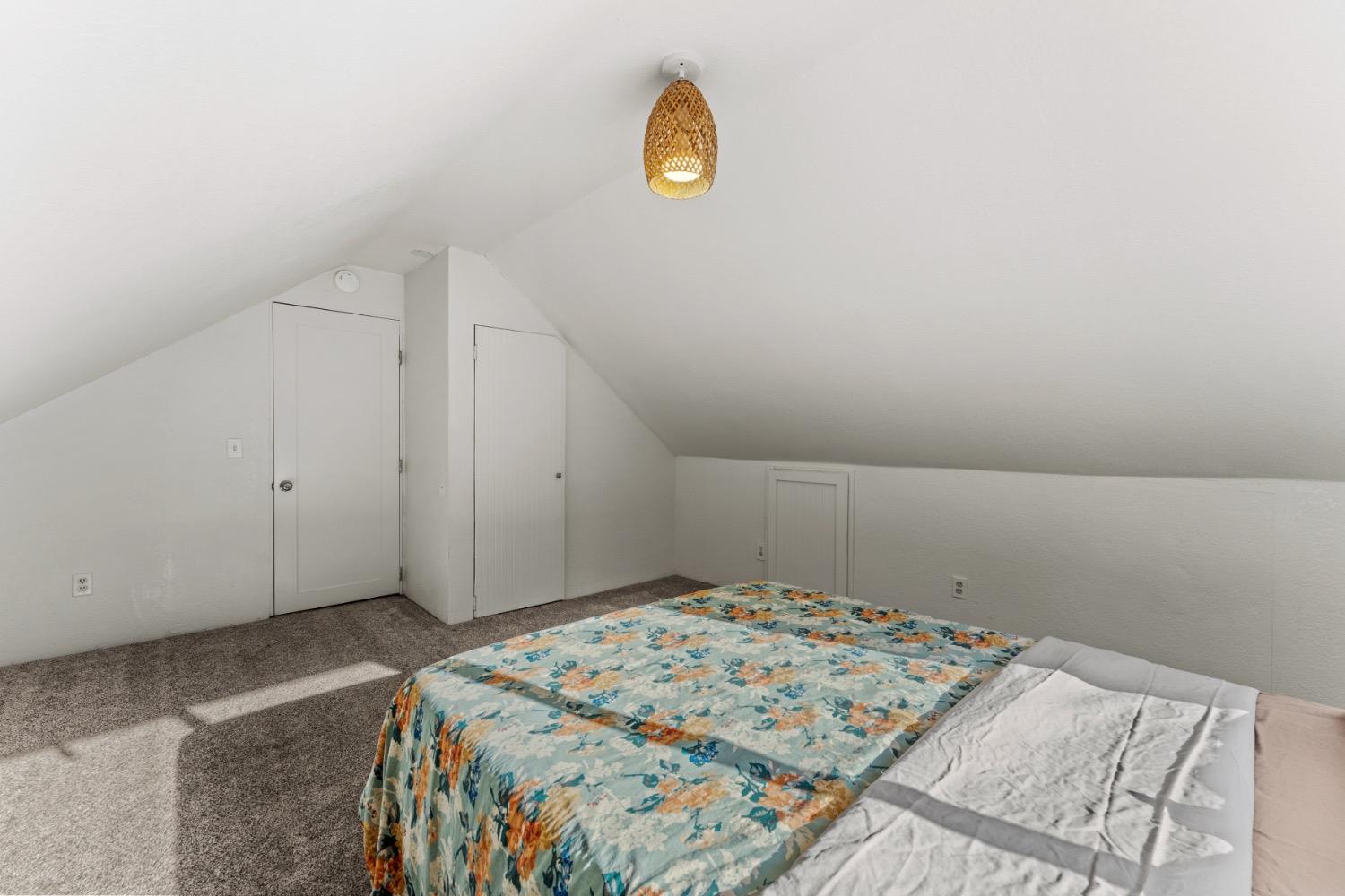 Attic bedroom with a colorful floral quilt on the bed and a woven pendant light.