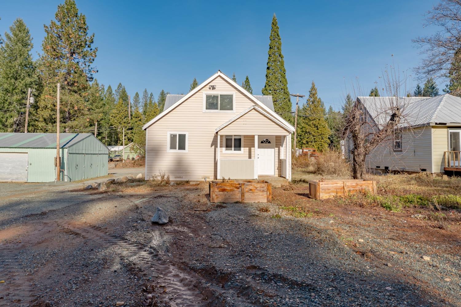 Beige gable-roofed house with a covered entry and raised planter boxes in a gravel yard.