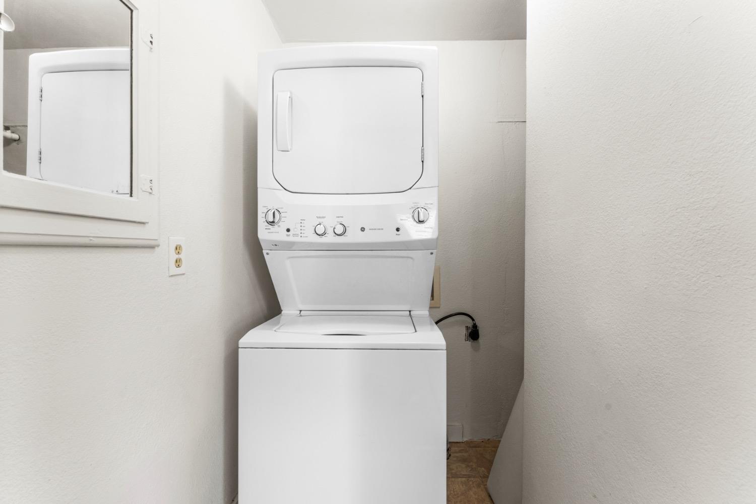 Stacked white washer and dryer in a compact laundry area beside a wall mirror.