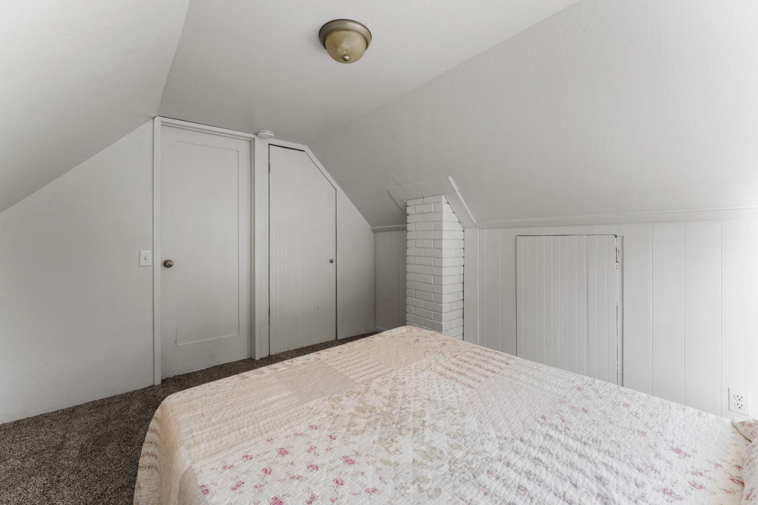 Upstairs bedroom with a floral quilted bed, sloped ceiling, and white brick chimney.