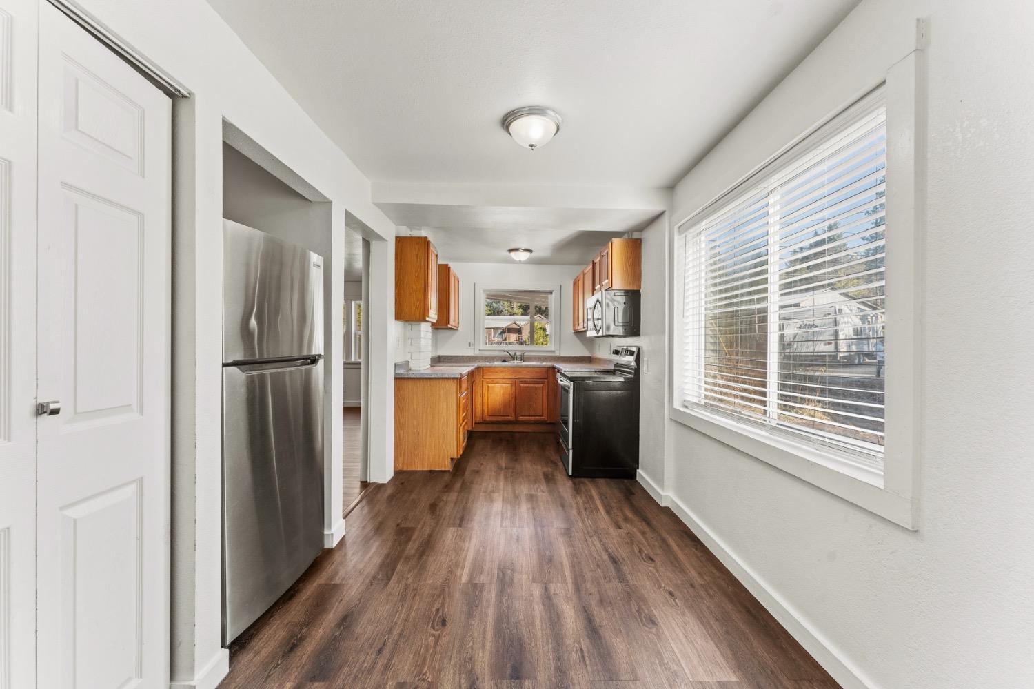 Kitchen with warm wood cabinets, stainless steel refrigerator, dark range, and a large window.
