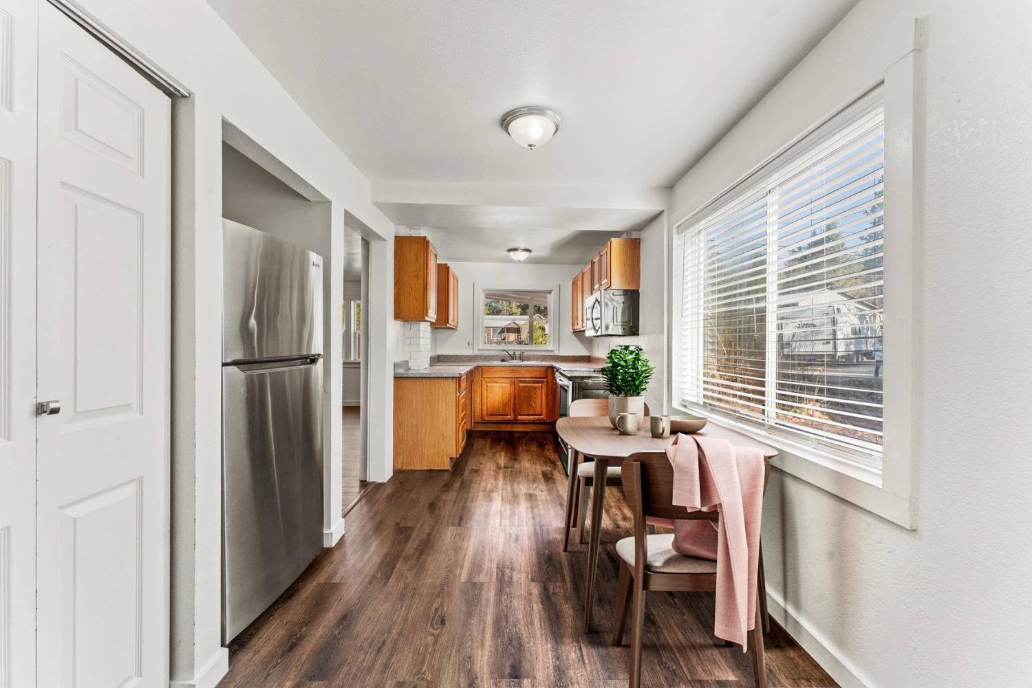 Kitchen with warm wood cabinets, stainless appliances, and a dining table beside a large window.