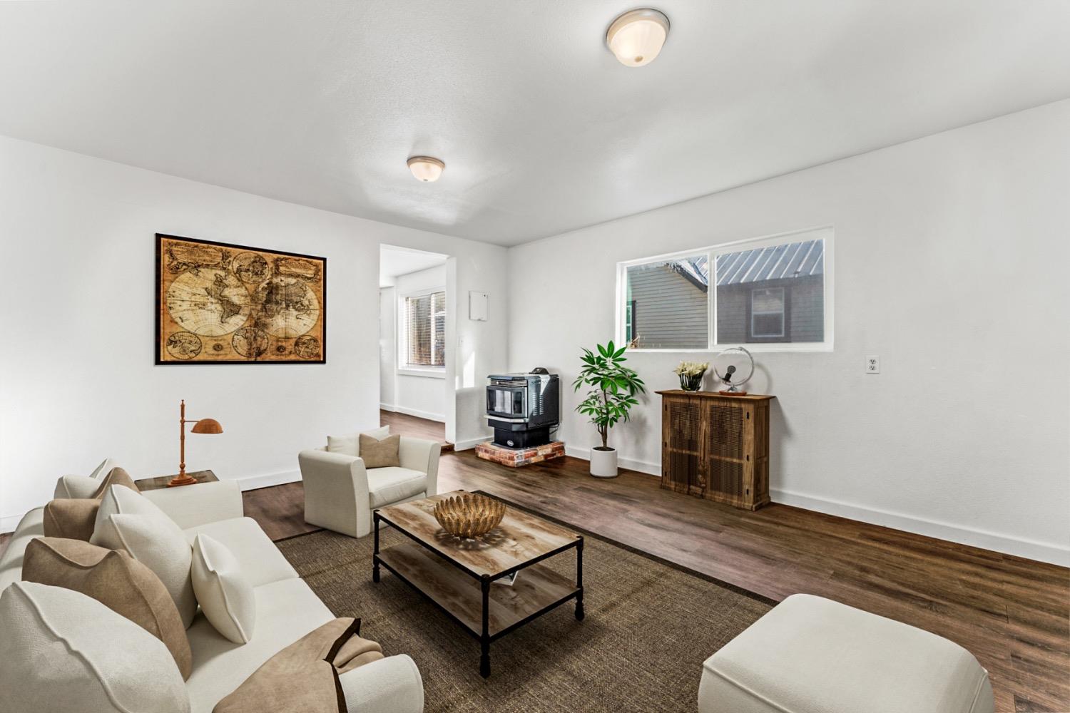 Staged living room with white seating, dark wood-look floors, and a freestanding stove.