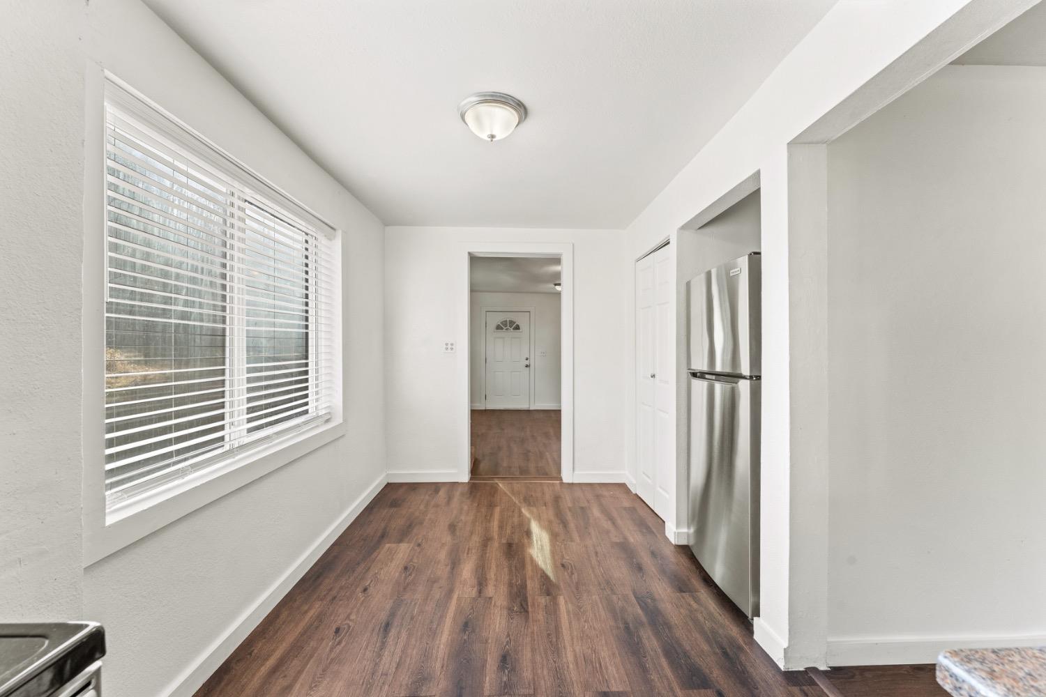 Narrow kitchen with dark wood-look floors, a stainless steel refrigerator, and a large window with blinds.