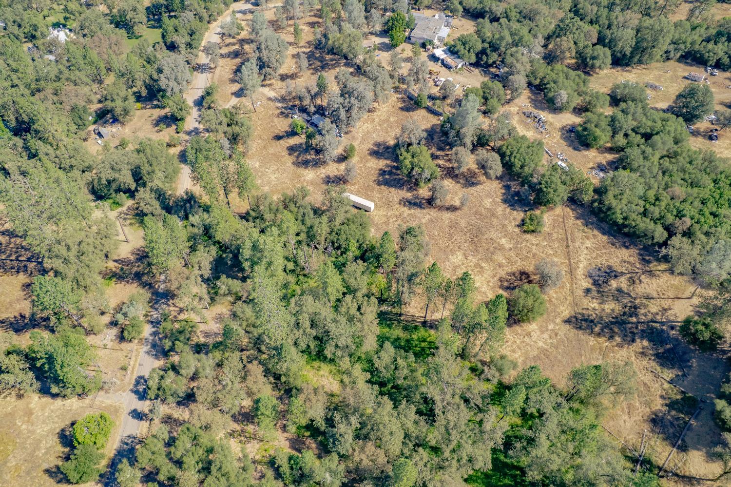 Aerial view of a partly cleared rural property surrounded by trees, with a road and scattered buildings.