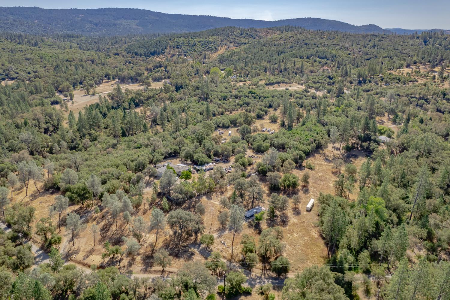 Aerial view of a wooded rural property with scattered homes and open clearings beneath distant hills.