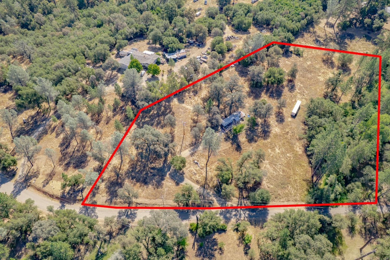 Aerial view of a wooded rural property outlined in red, with a small home and roadside frontage.